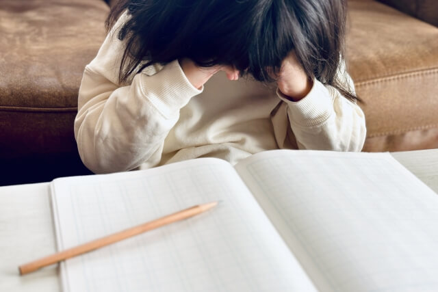 夏休み明け、無造作に広げたノートと鉛筆が載っている机、泣いている女の子